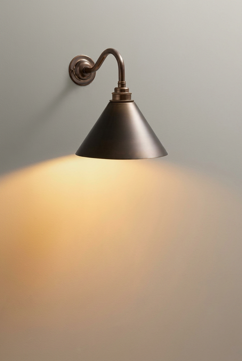Antique bronze cone sconce with veined marble backplate, casting a warm halo across a soft plaster wall